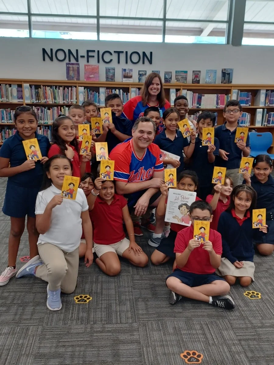 Group of children holding books in a library next to two adults, with a 'Non-Fiction' sign on the wall behind them.
