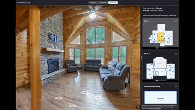 A spacious living room with wooden walls and ceiling, large windows, hardwood floor, a stone fireplace, and multiple sofas arranged around the room.
