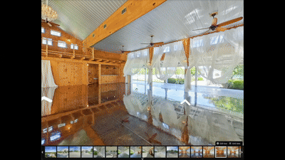 Interior view of a wooden house with large windows, a pool outside, and a shiny wooden floor reflecting the ceiling and walls.