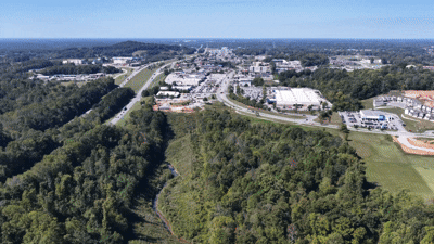 Aerial view of a suburban area surrounded by trees, with roads and buildings visible in the distance.