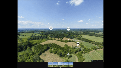 Aerial view of a vast green landscape with fields and forests under a blue sky with clouds, viewed through a computer interface with photo markers.