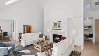 Living room with white sofas, a wooden coffee table, a fireplace, a painting on the wall, and a blue armchair.