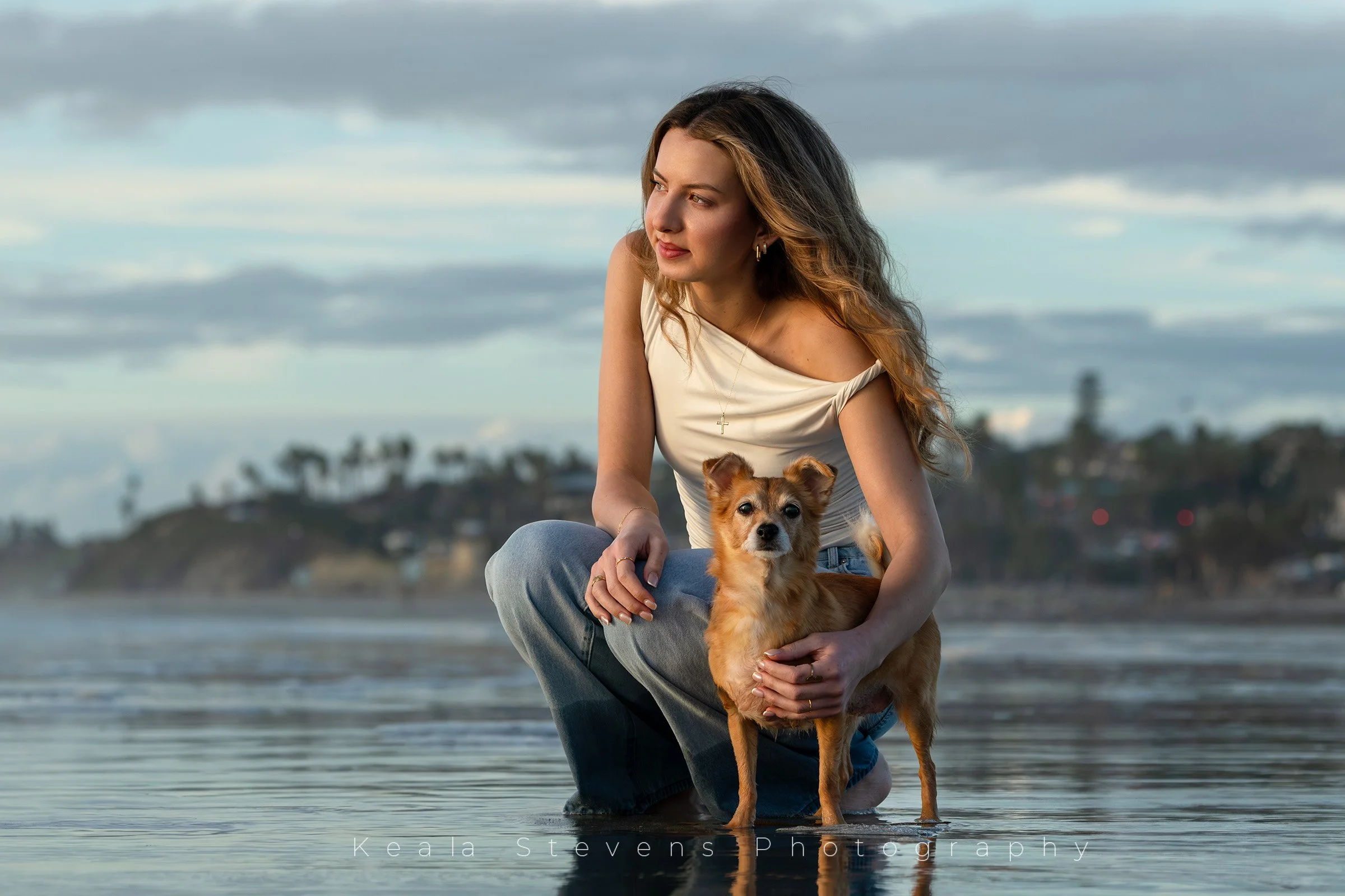 A woman watches the sunset with her dog at the beach.