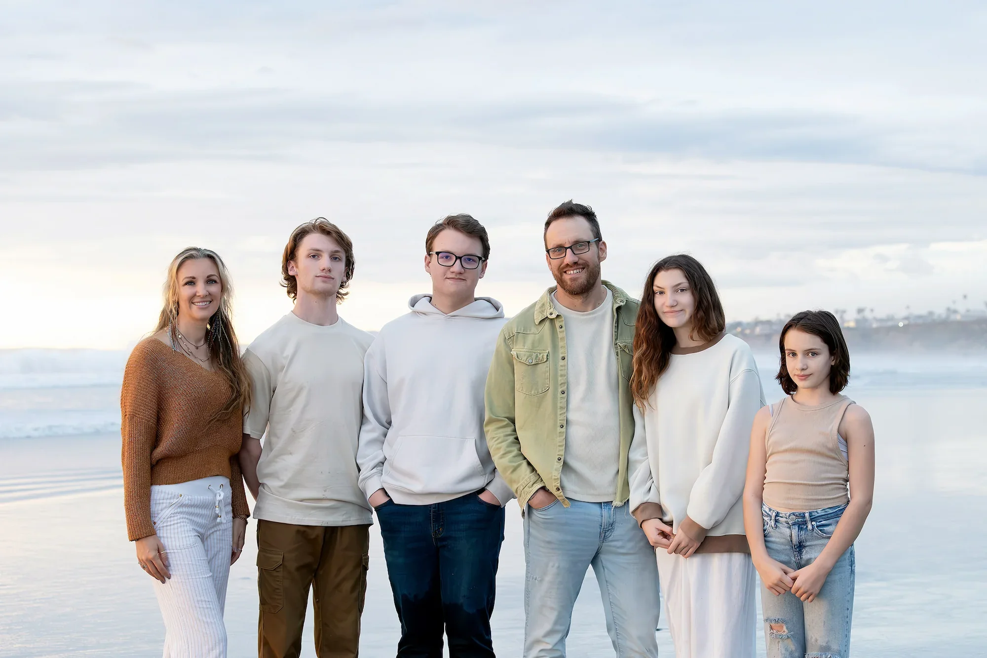 a family of six stand posing for photos at the beach.