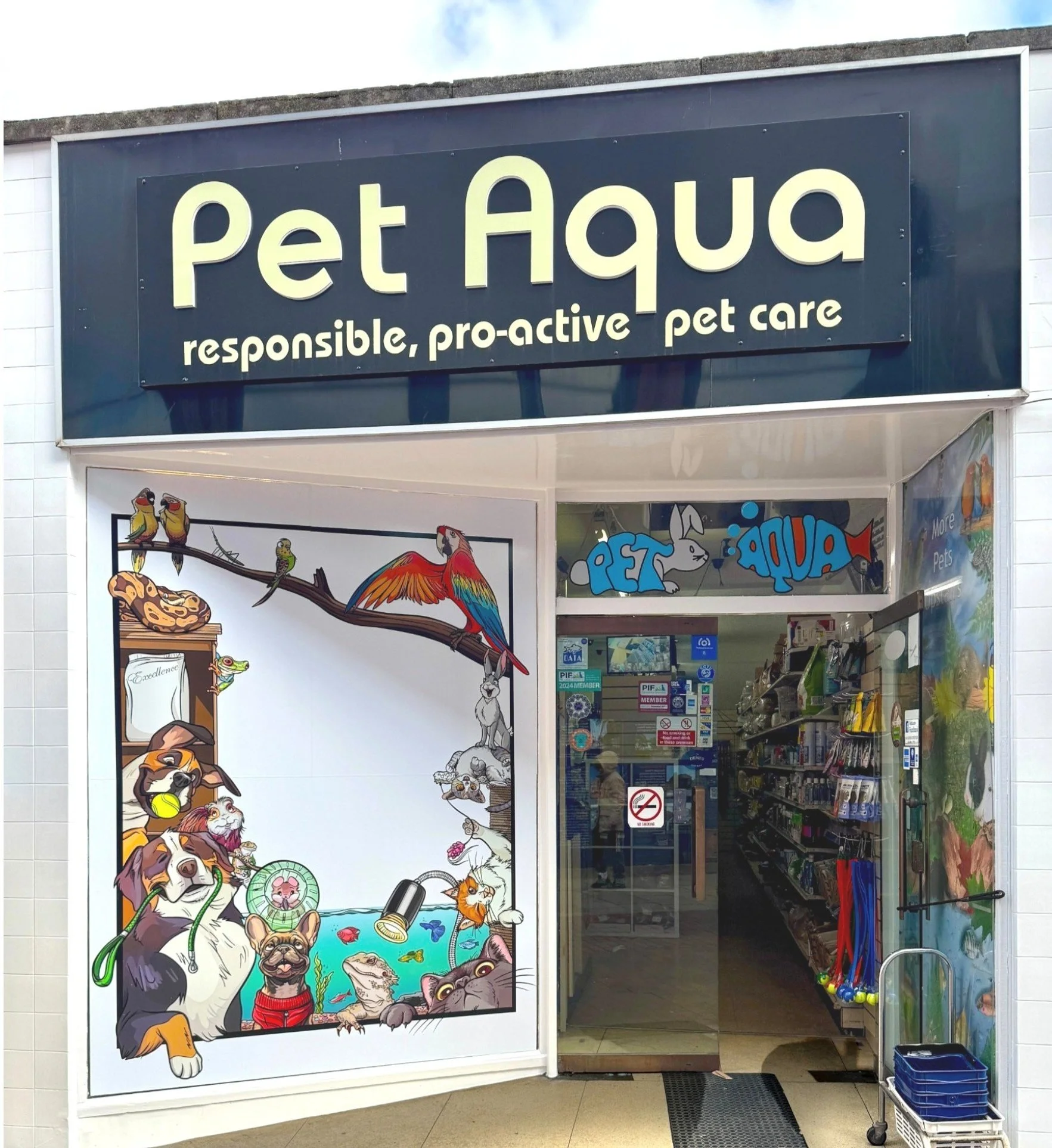 Storefront of Pet Aqua with signage reading 'responsible, pro-active pet care'. The window features an colorful illustration of various pets including dogs, cats, birds, and reptiles around a fish pond, and the interior is visible through the glass, showing pet supplies and equipment.