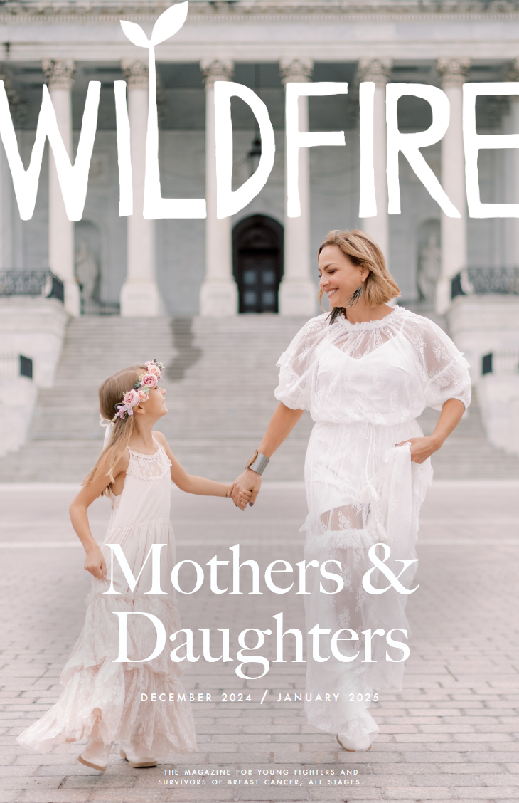 A mother and daughter holding hands and smiling in front of a government building with stairs, wearing white dresses, with the text "Wildfire" and "Mothers & Daughters" on the cover of a magazine for young fighters and survivors of breast cancer.