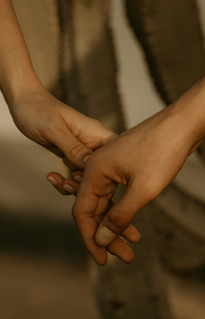 Close-up of two people holding hands, with one person's hand overlapping the other's, against a blurred background.