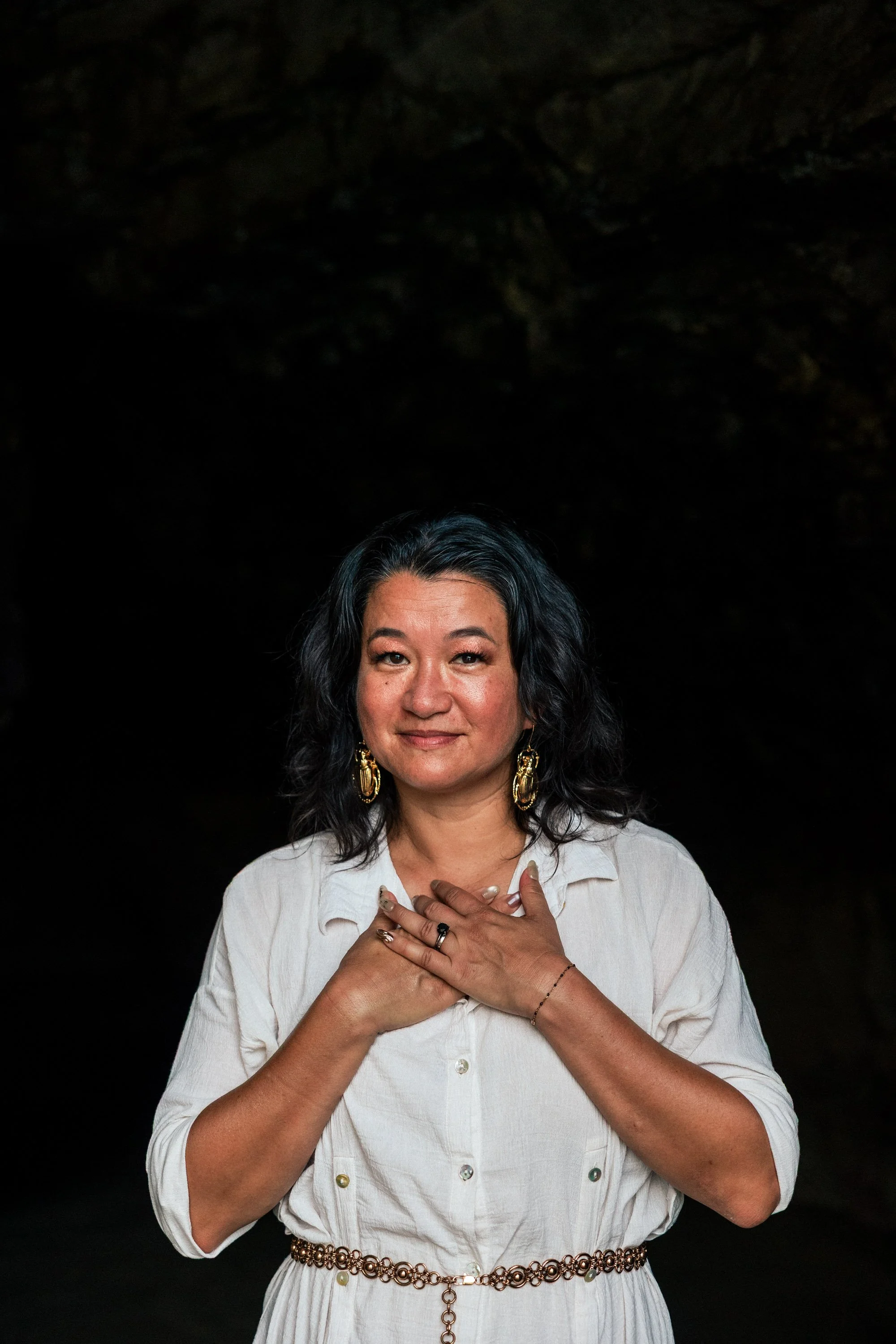 Leslie Levito standing in front of a dark cave with both hands over her heart