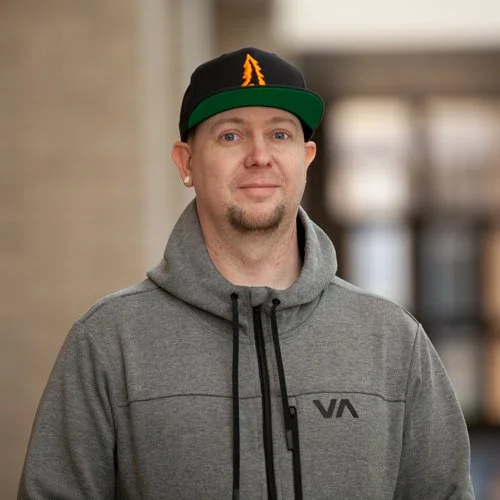 Man wearing a gray hoodie and a black cap indoors