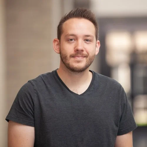 A man with short hair and a beard wearing a dark gray t-shirt.