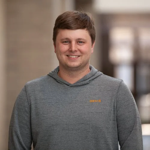 Smiling person wearing a gray Orvis hoodie indoors.