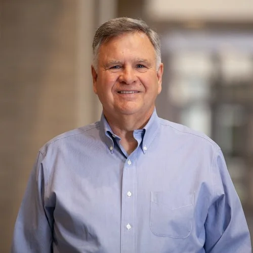 Smiling man wearing a light blue button-up shirt indoors.