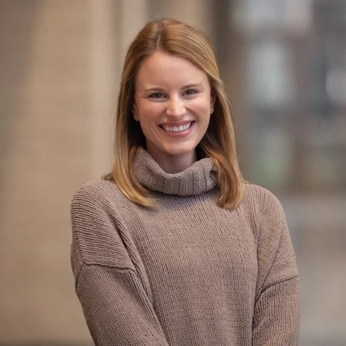 Woman smiling in a sweater indoors with a blurred background.