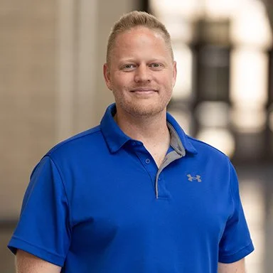 Person wearing a blue polo shirt with a blurred urban background.