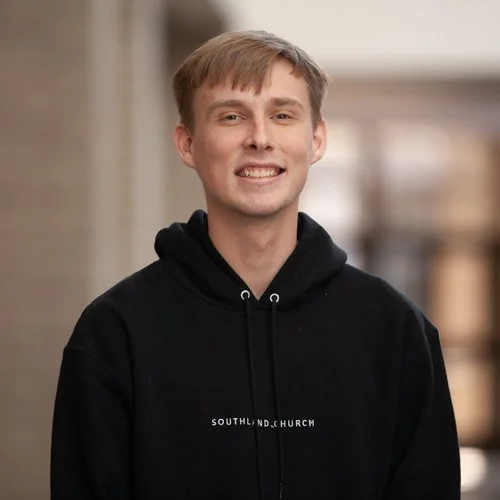 Young man wearing a black hoodie with "Southland Church" printed on it, standing indoors and smiling at the camera.