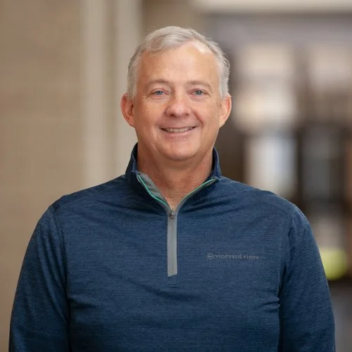 Man smiling at the camera, wearing a blue Vineyard Vines pullover, standing indoors.