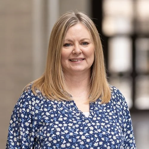 Smiling woman with long blonde hair wearing a blue floral patterned shirt