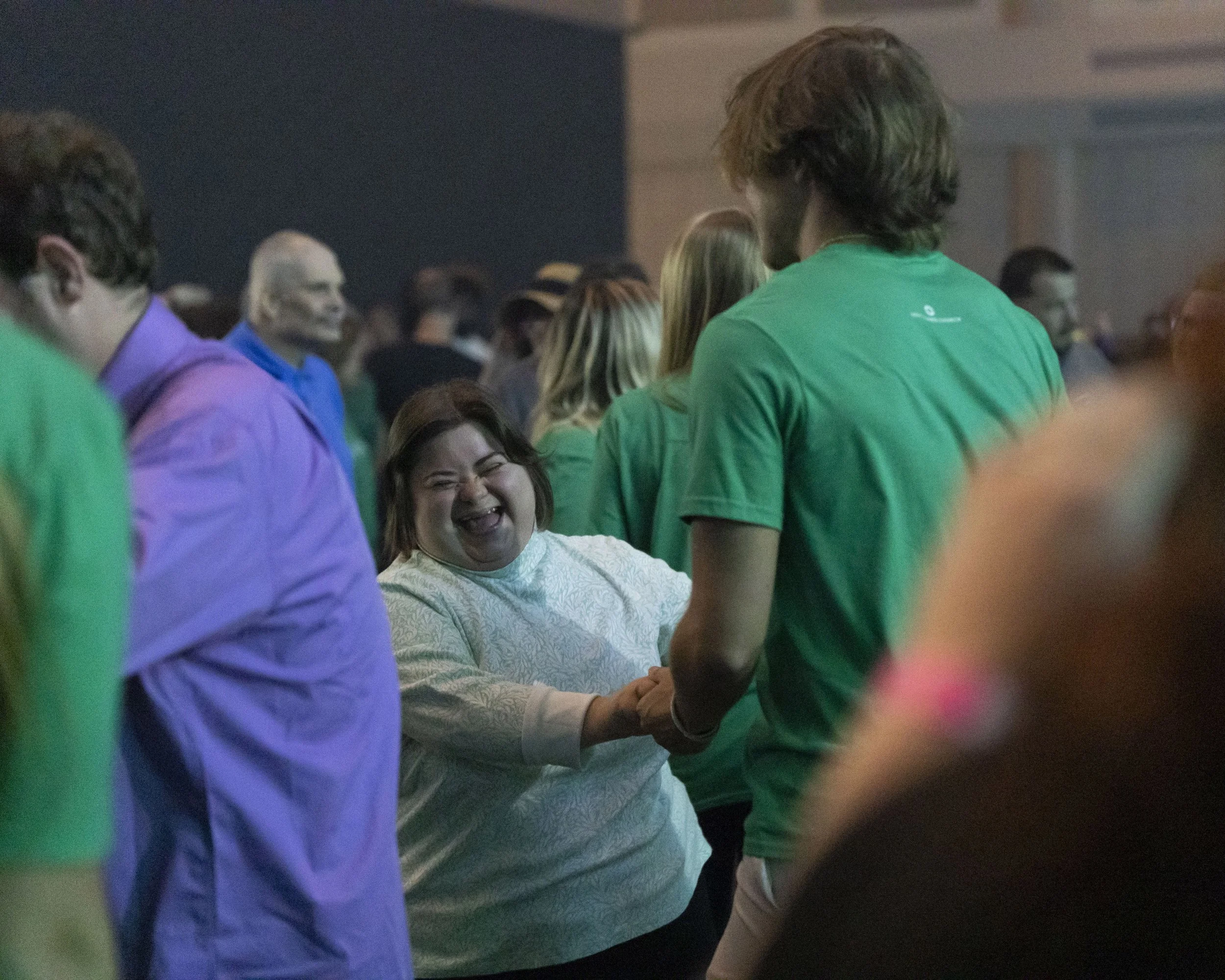Group of people wearing colorful shirts at a social event, with one individual smiling and holding hands with another.