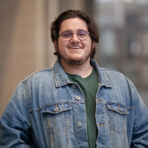 Person wearing glasses and a denim jacket indoors