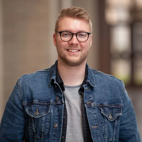 Man wearing glasses and a denim jacket smiling indoors