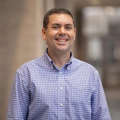 Smiling man in a checkered shirt standing indoors