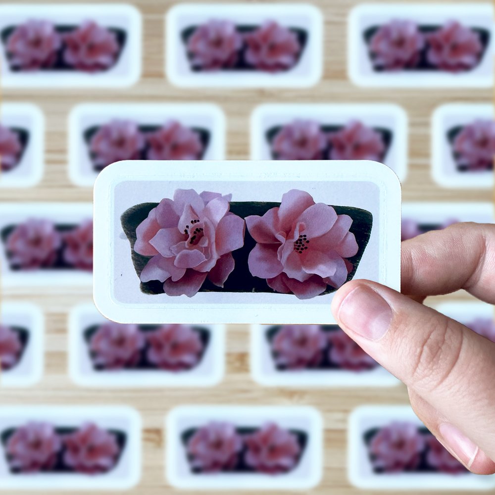 Hand holding a sticker of two pink flowers