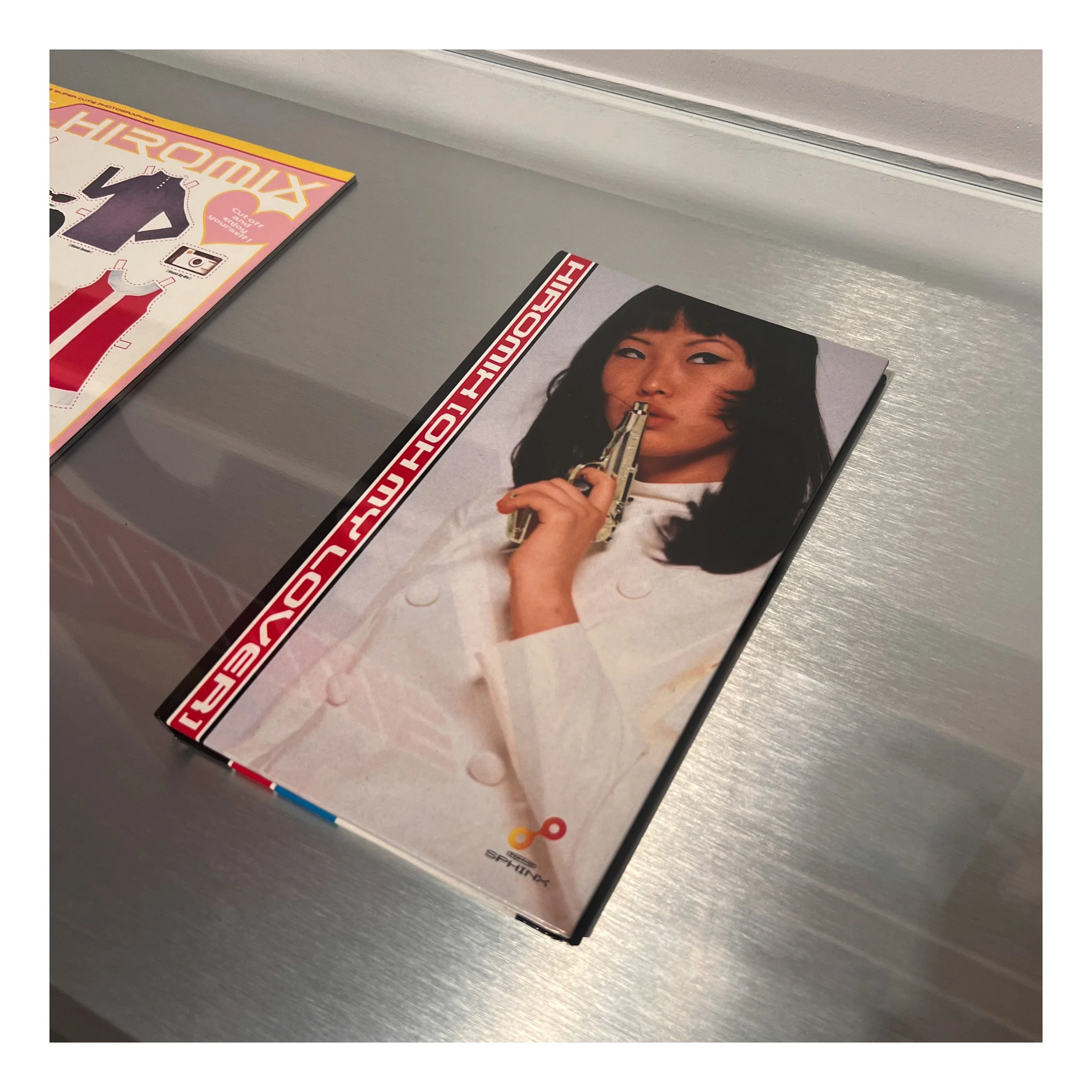 Part of a magazine or book titled 'Hiroshima' with a woman's face holding a gun on the cover, and a partially visible magazine or booklet titled 'Chromix' on a gray surface.