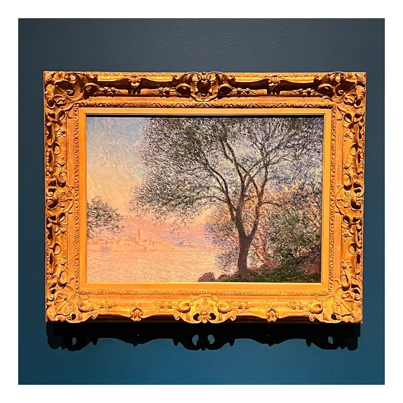 Painting of a tree with sparse leaves next to a body of water, with a colorful sky in the background, in an ornate gold frame.