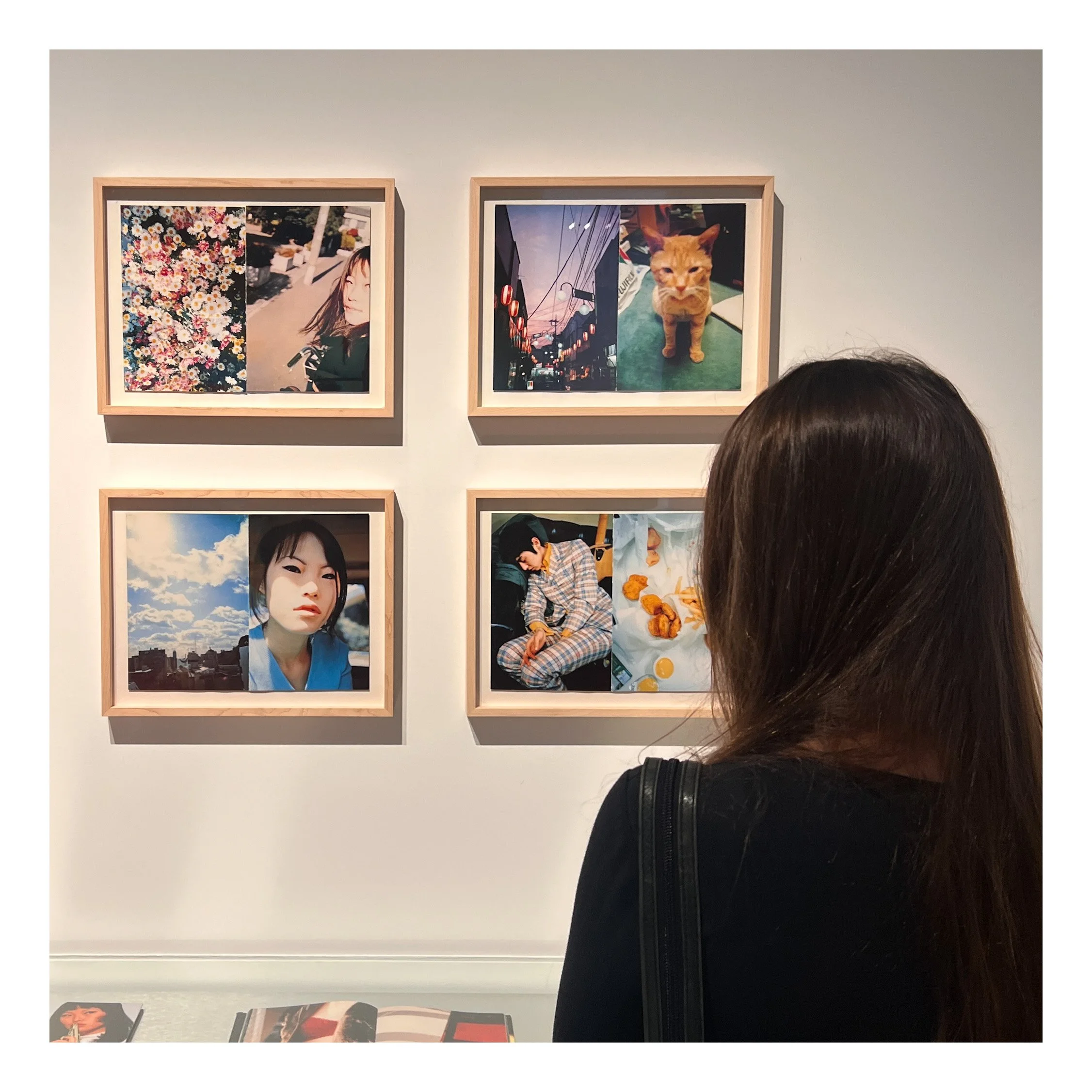 Photo of art gallery wall with framed photographs, including a city scene with hanging lights and a portrait of a woman, viewed with person’s head in foreground.