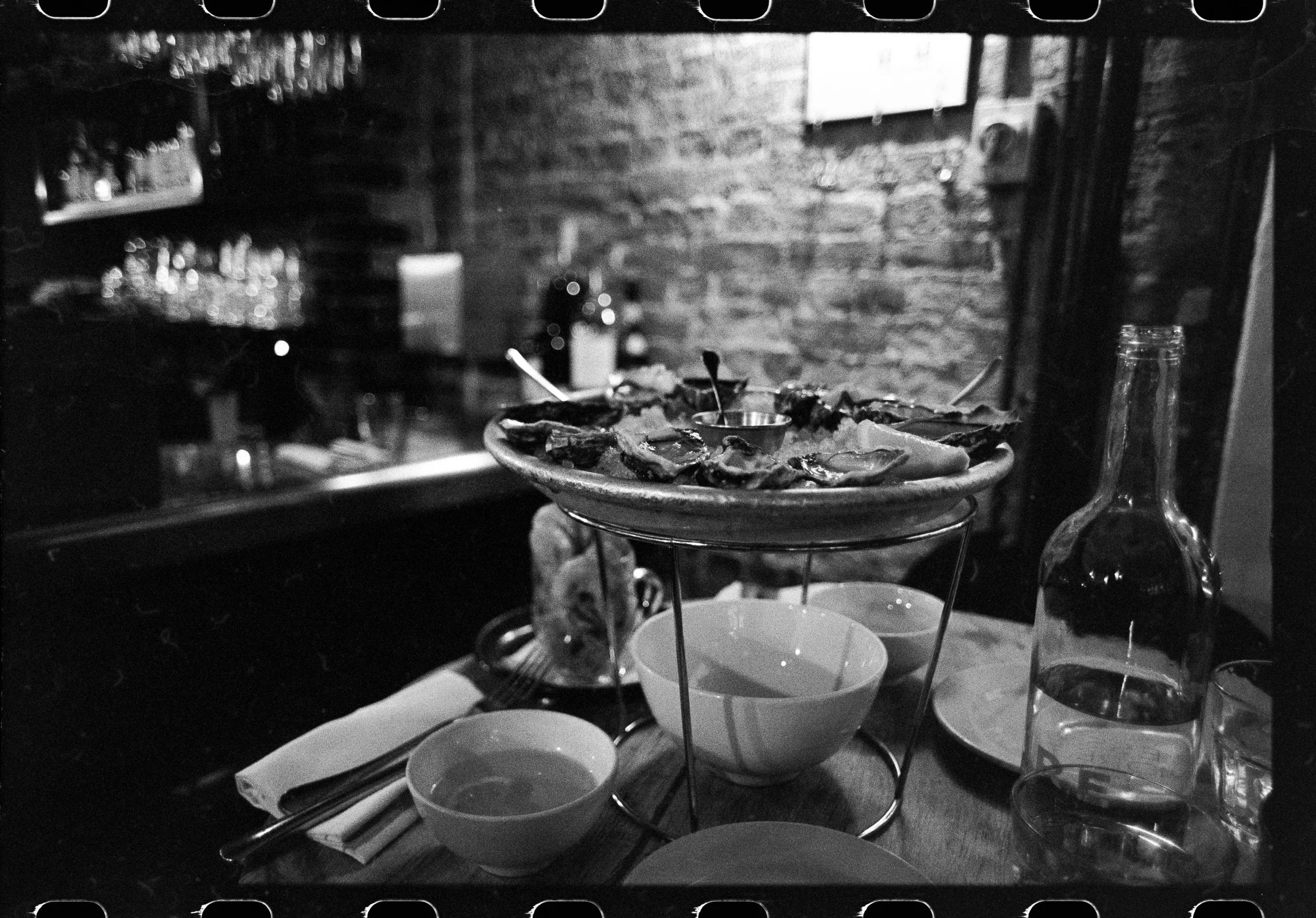 A pizza on a raised stand inside an oven, surrounded by bowls and bottles, in a cozy restaurant setting with brick walls.