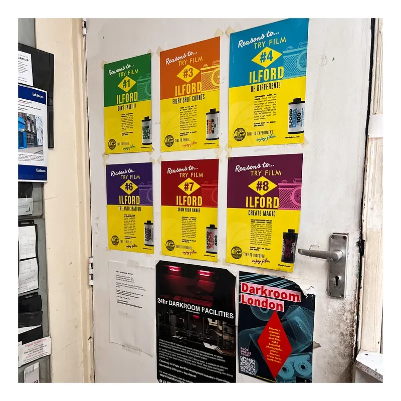Colorful posters on a wall advertising film testing reasons, numbered #1 to #8, with each poster highlighting a different reason to try film, such as 'Don't Fake It,' 'Every Shot Counts,' 'Be Different,' 'The Anticipation,' 'Share Your Range,' and 'C