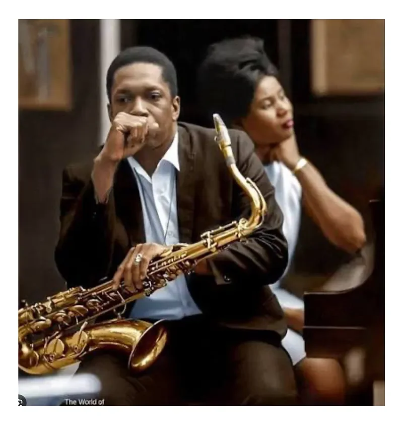 A man holding a saxophone sitting next to a woman in an indoor setting, both with serious expressions.