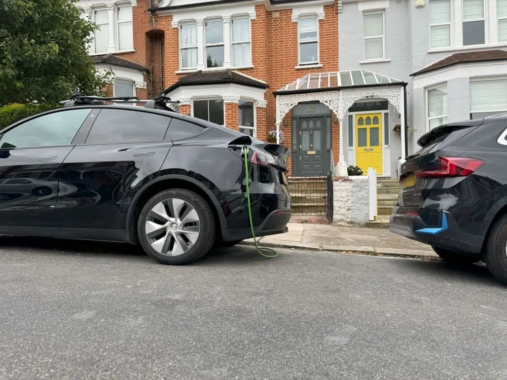 Black EV being charged on roadside of terraced street