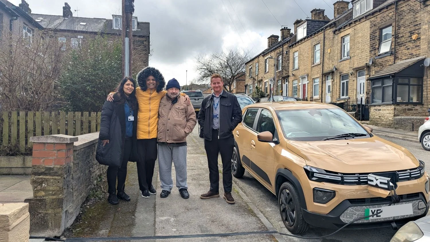 4 people in coats stood on pavement next to EV being charged on the street outside house
