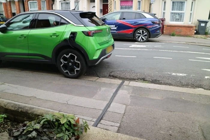Green Electric car parked on street beside cross pavement EV cable gully