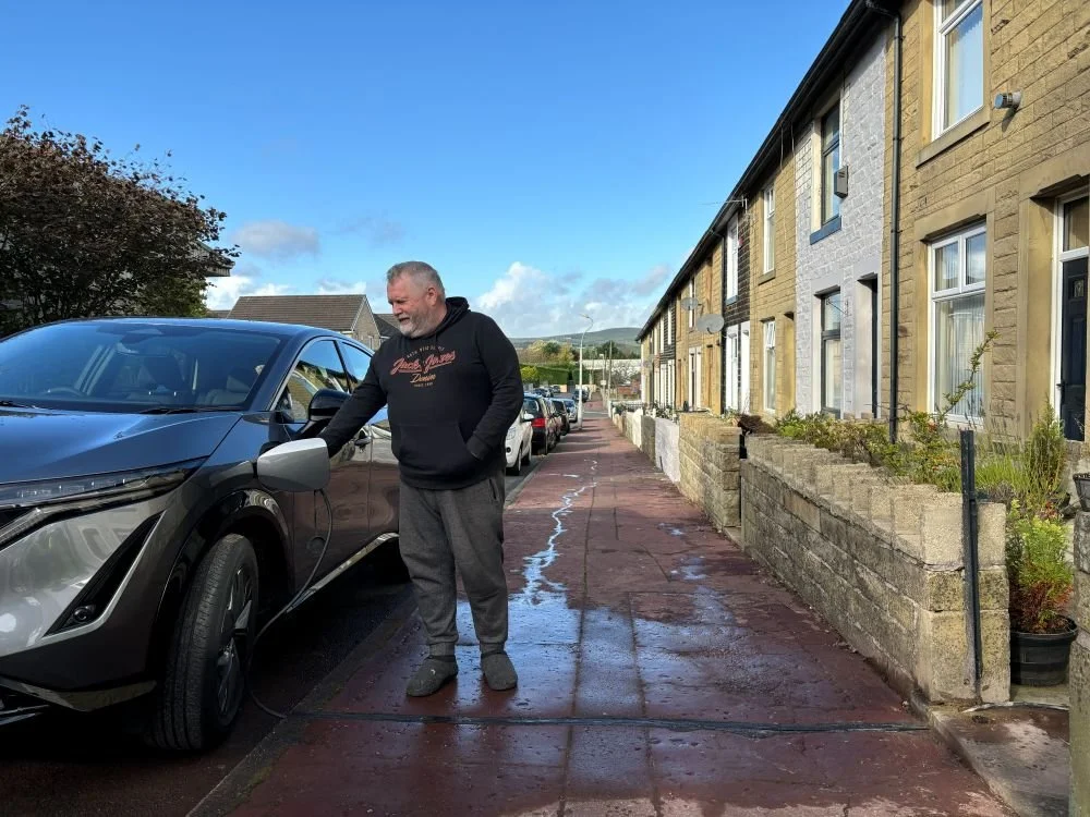 Man charging car which is parked on the side of the road outside terraced house
