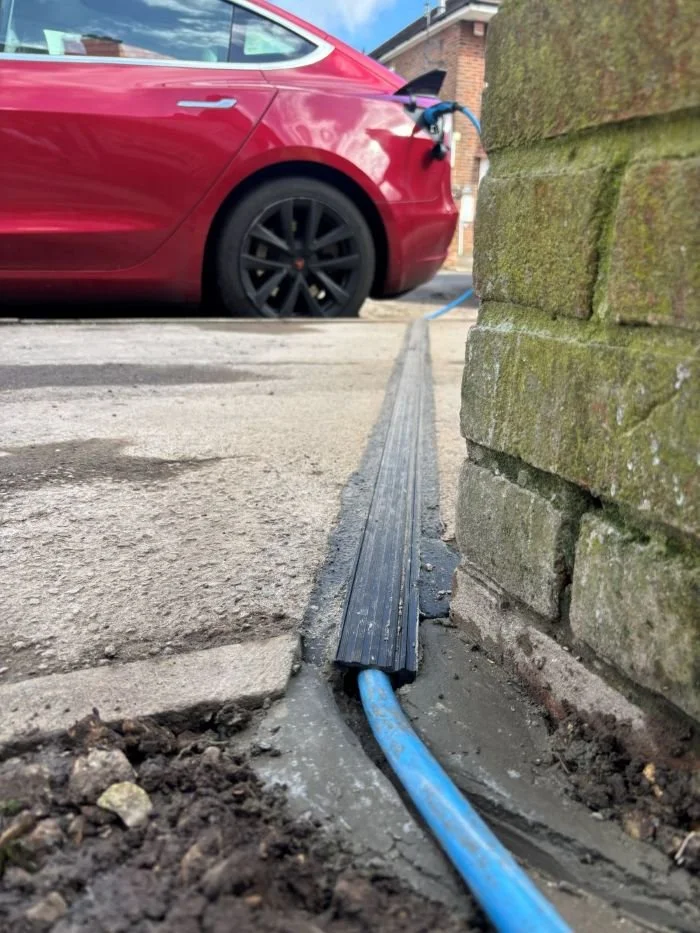 blue EV Cable tucked into gully in pavement to charge car parked on residential street