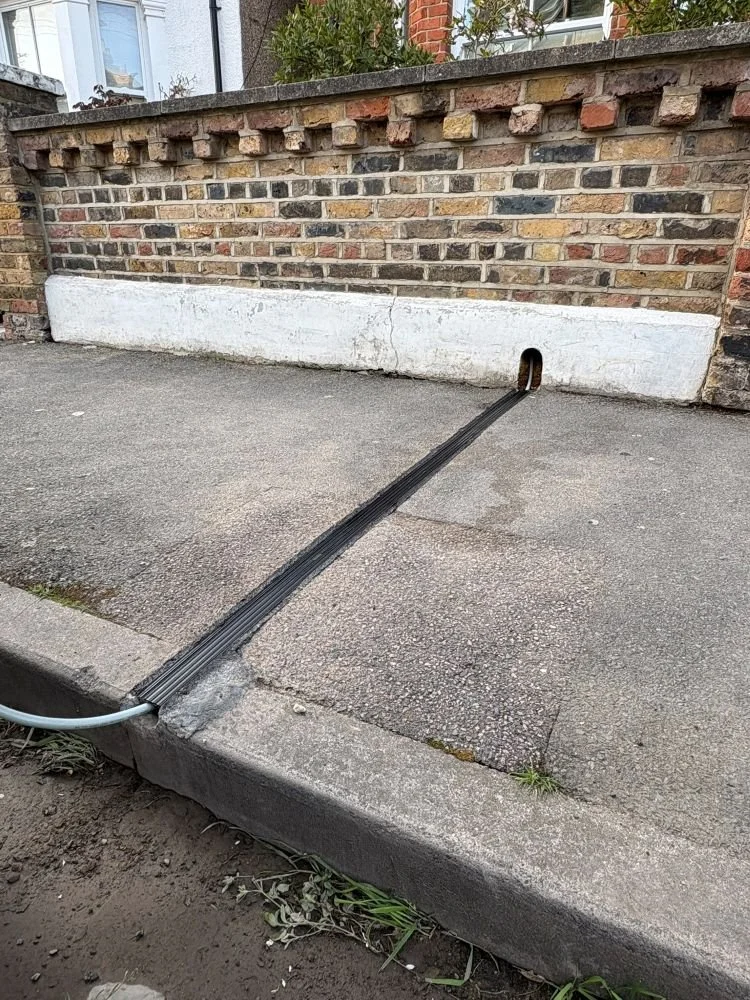 EV cable channel with EV charger cable running through hole in wall to the edge of the pavement