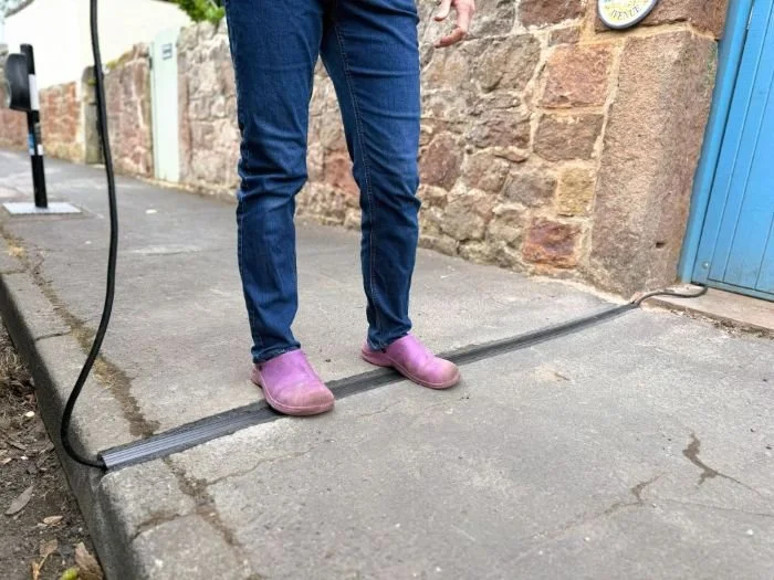 person in purple crocs and blue jeans standing on top of cross pavement ev cable gully