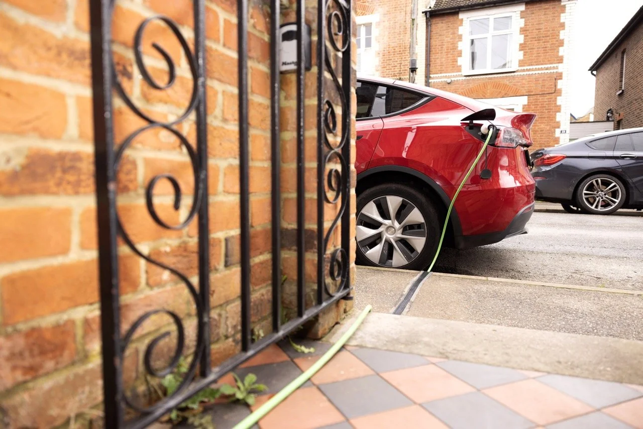 EV charger cable running along side front gate across pavement and into a red electric car