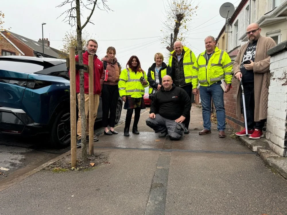 Group of people facing camera standing next to EV charger gully in pavement in Coventry