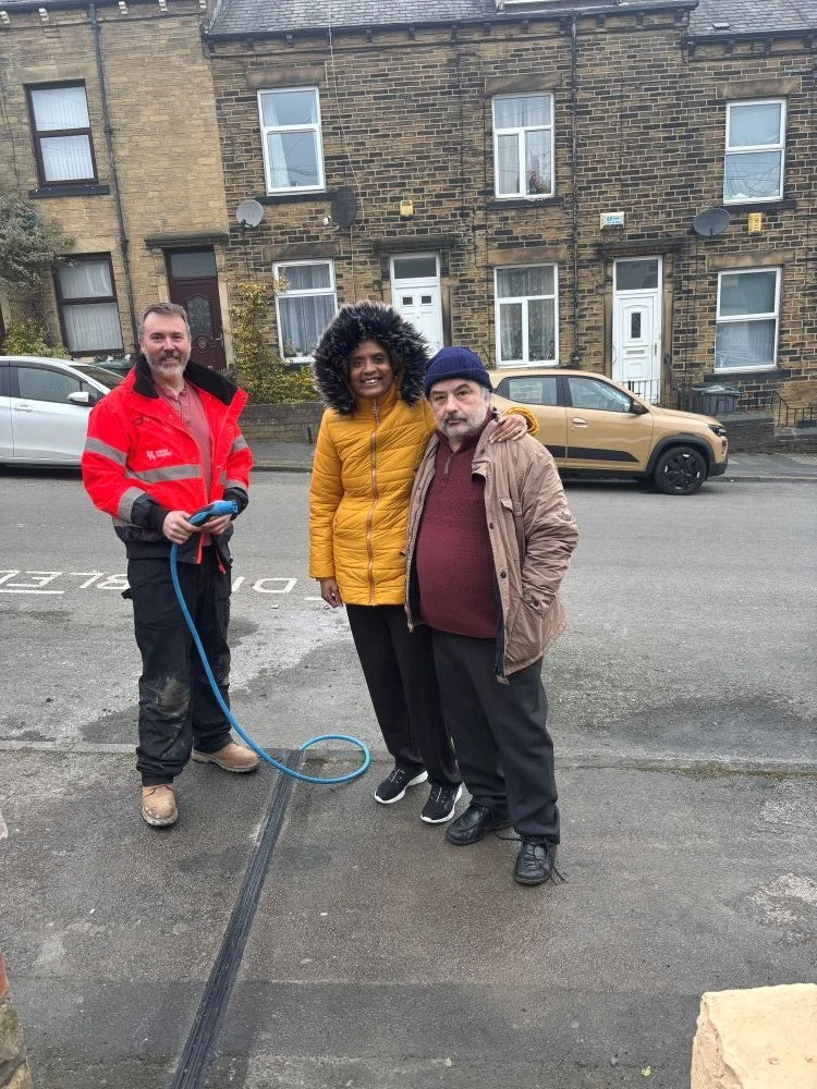 3 people stood on pavement next to EV cable channel with one man in high vis holding EV cable