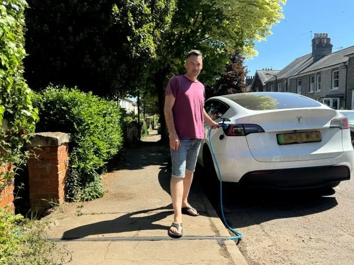 man in shorts, tshirt and sandles charging white car parked on street