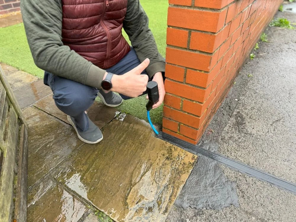 Man crouching down next to cross-pavement charging system installed in Bolton