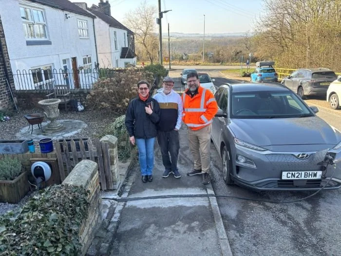 3 people stood on pavement next to EV being charged on the street