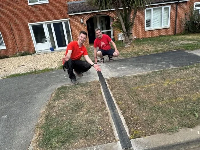 two men crouched down beside EV gully channel across the pavement