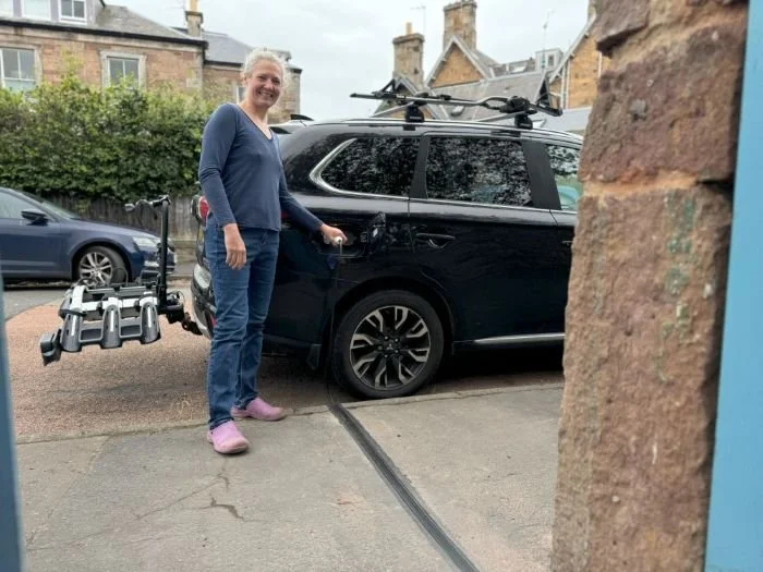 lady in blue jeans and jumper charging car parked on side of the road