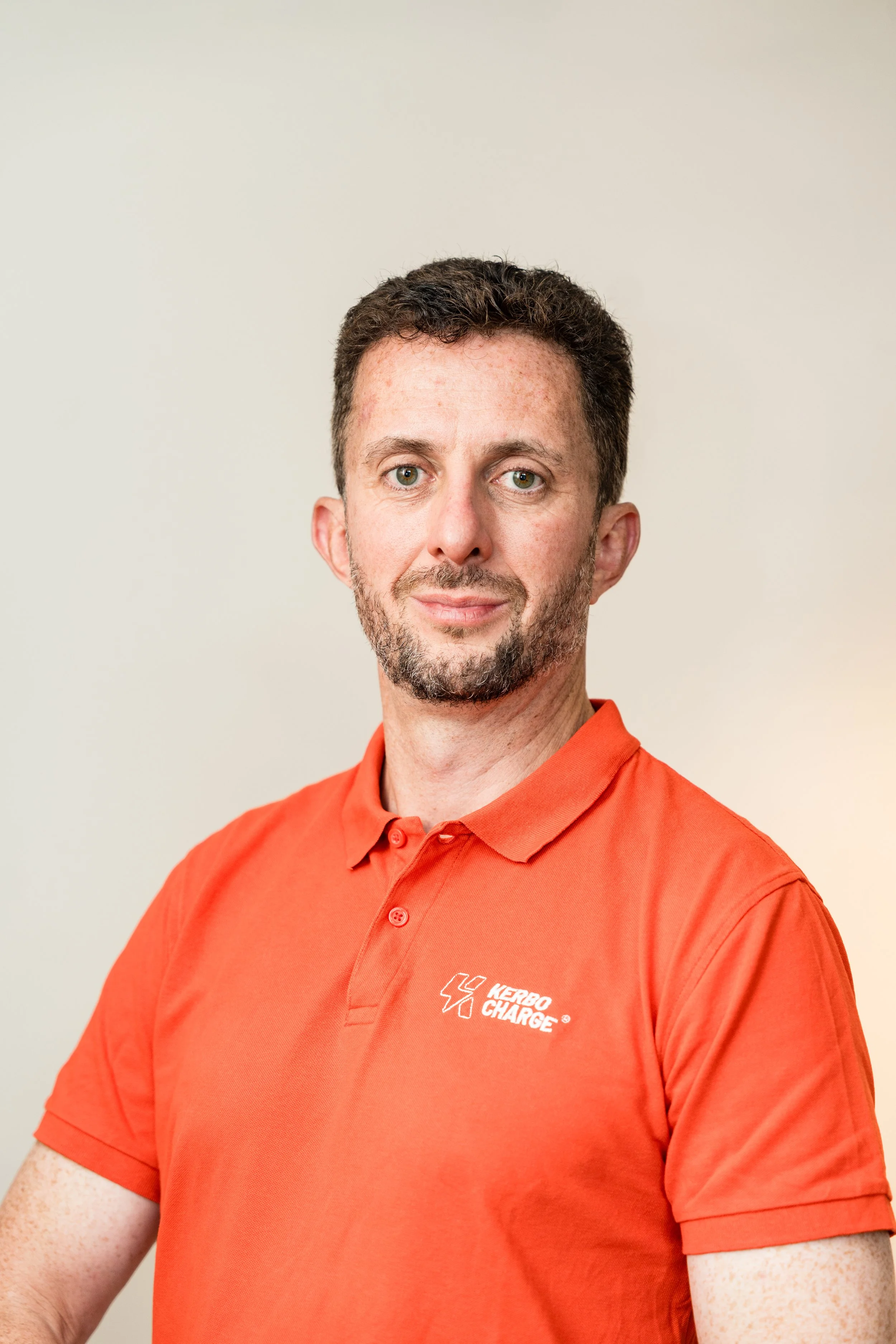 A man wearing a red polo shirt with a 'Kerbo Charge' logo, standing against a plain background.