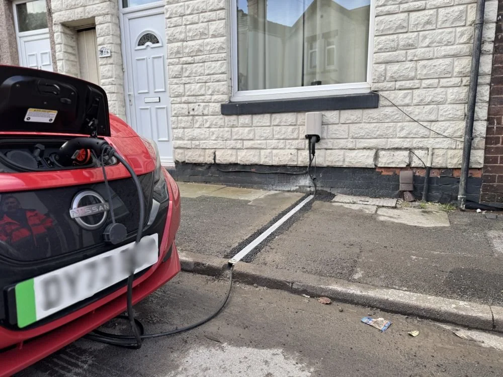 Red EV parked on roadside outside terraced house being charged via a cable gully in the pavement