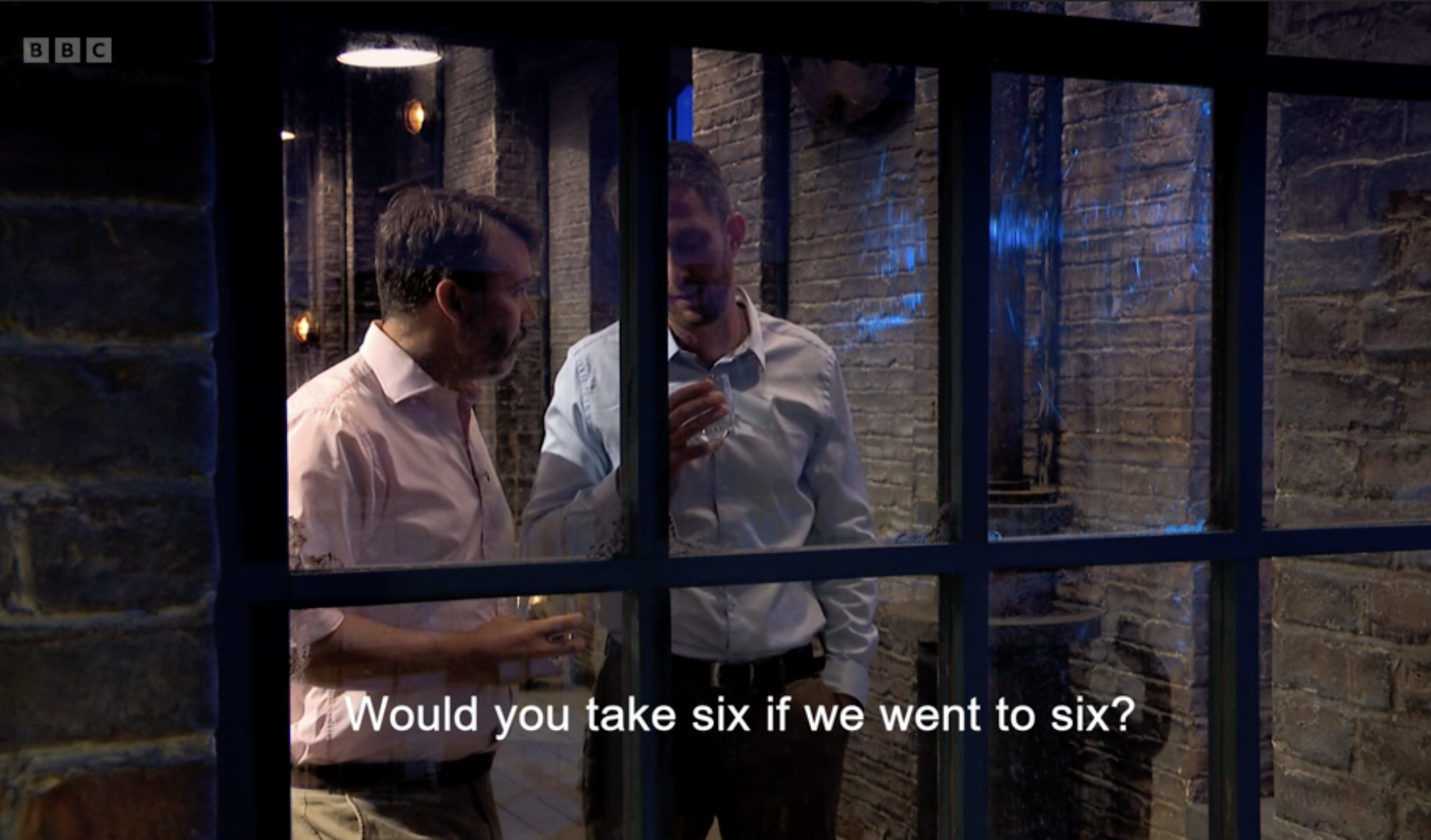 Two men in dress shirts having a conversation, seen through a window with a brick wall background at night. Subtitles read: "Would you take six if we went to six?"